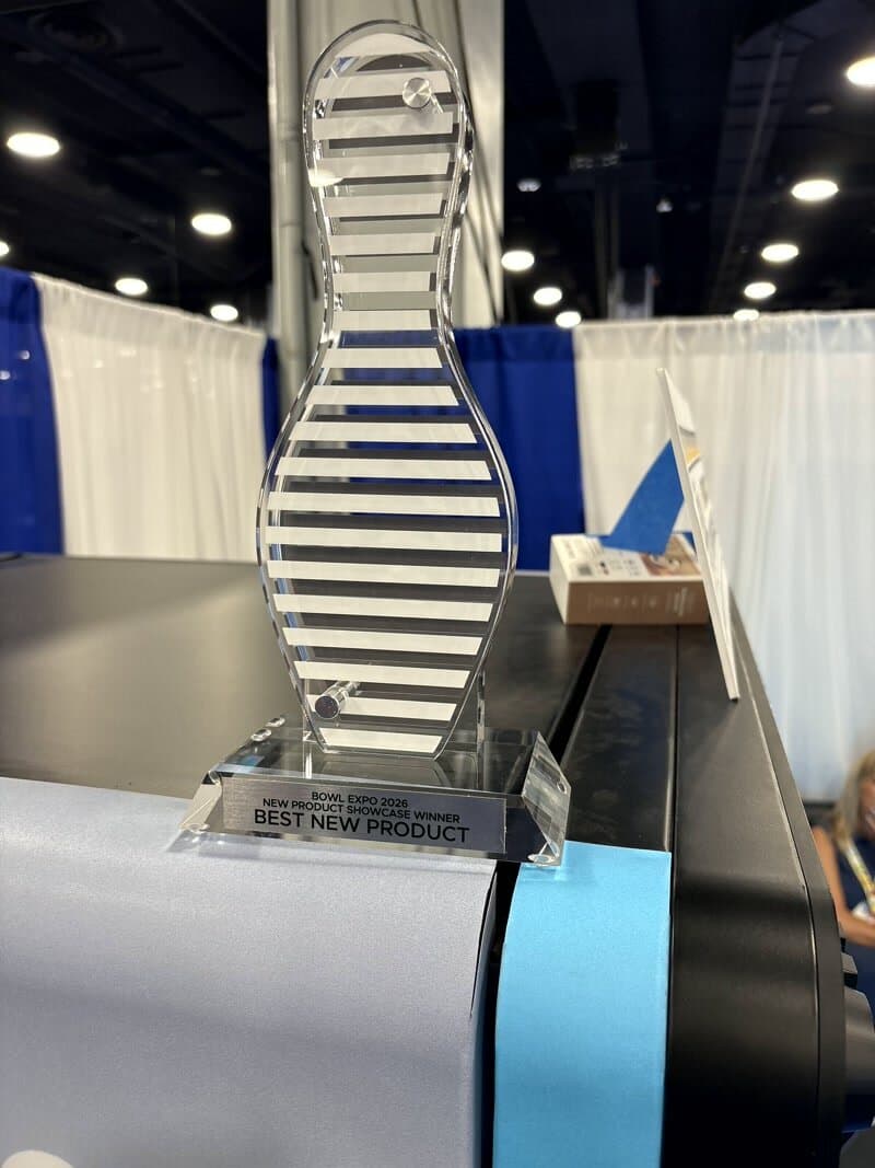 Bowl Expo 2026 New Product Showcase Winner trophy — an acrylic bowling pin engraved Best New Product — on top of a Custom Case Kiosk
