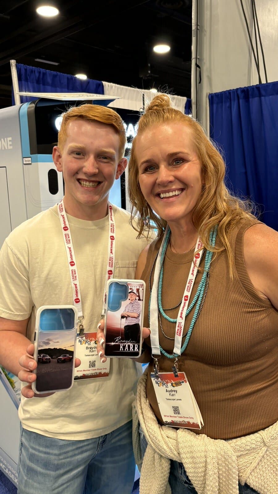 Two smiling Bowl Expo attendees holding up the custom photo cases they designed and printed at the booth
