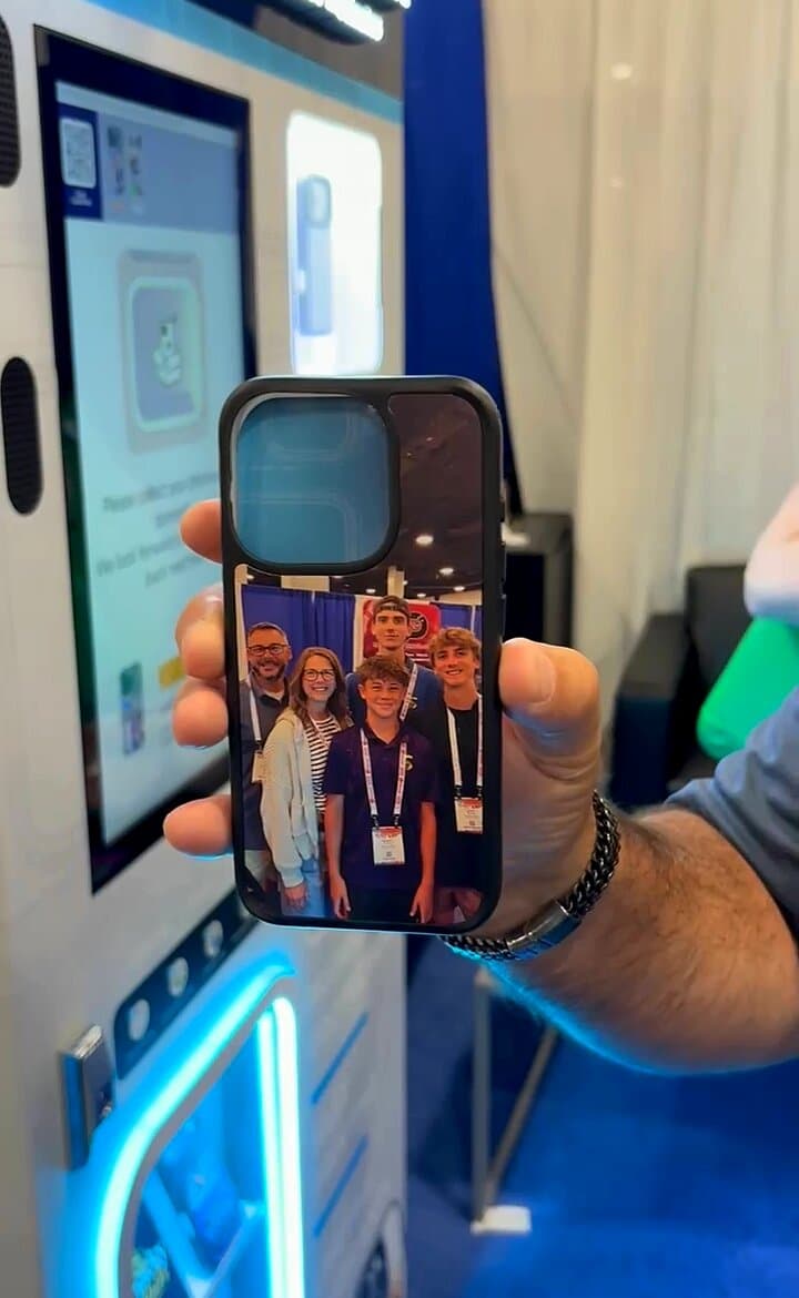 A just-printed clear iPhone case with a family photo held up in front of the Custom Case Kiosk