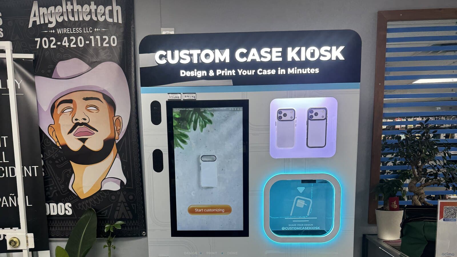 The Custom Case Kiosk inside Angel The Tech Wireless in North Las Vegas, its lit marquee above a touchscreen showing the Start customizing screen, with the store's banner on the wall beside it