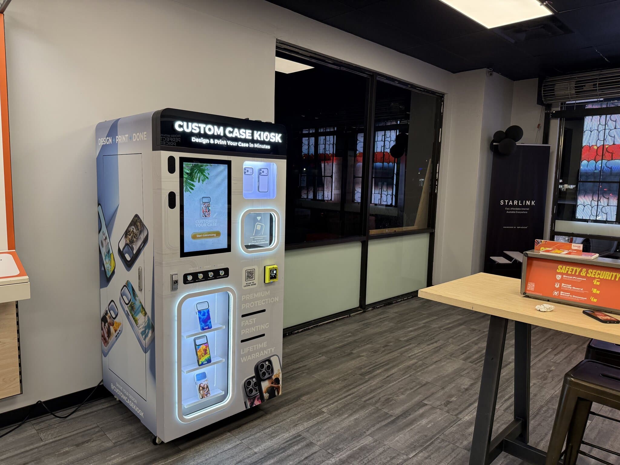 Custom Case Kiosk inside Boost Mobile on N 32nd St in Phoenix, Arizona — CCK-V4 unit with lit case shelves beside the store's high-top counter