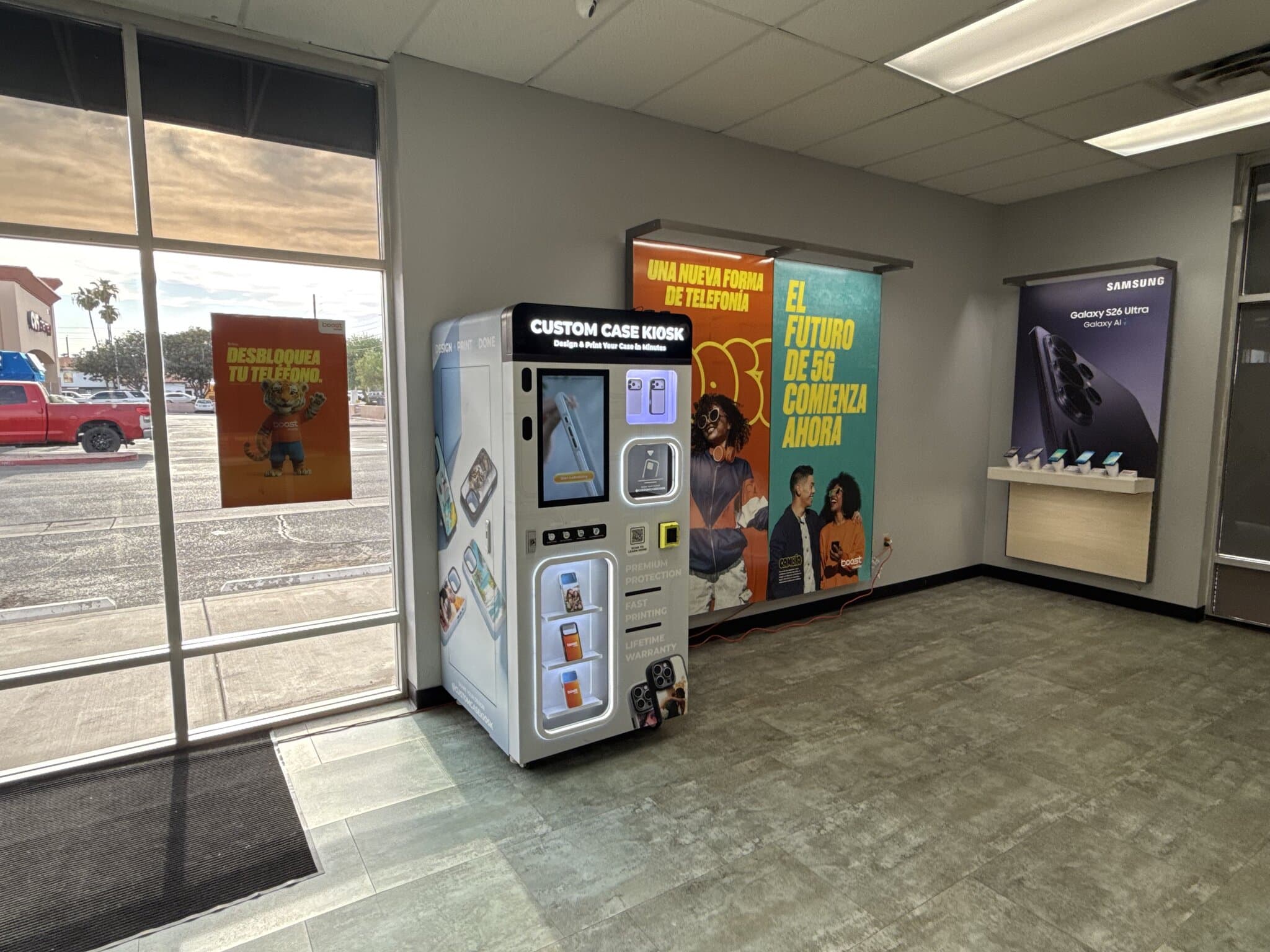 Custom Case Kiosk beside the storefront windows of the Boost Mobile store in Maryvale, Phoenix, with Boost banners and the Samsung display wall
